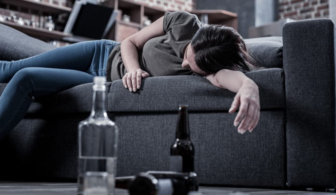 drunk woman sleeping on sofa with signs of alcohol addiction