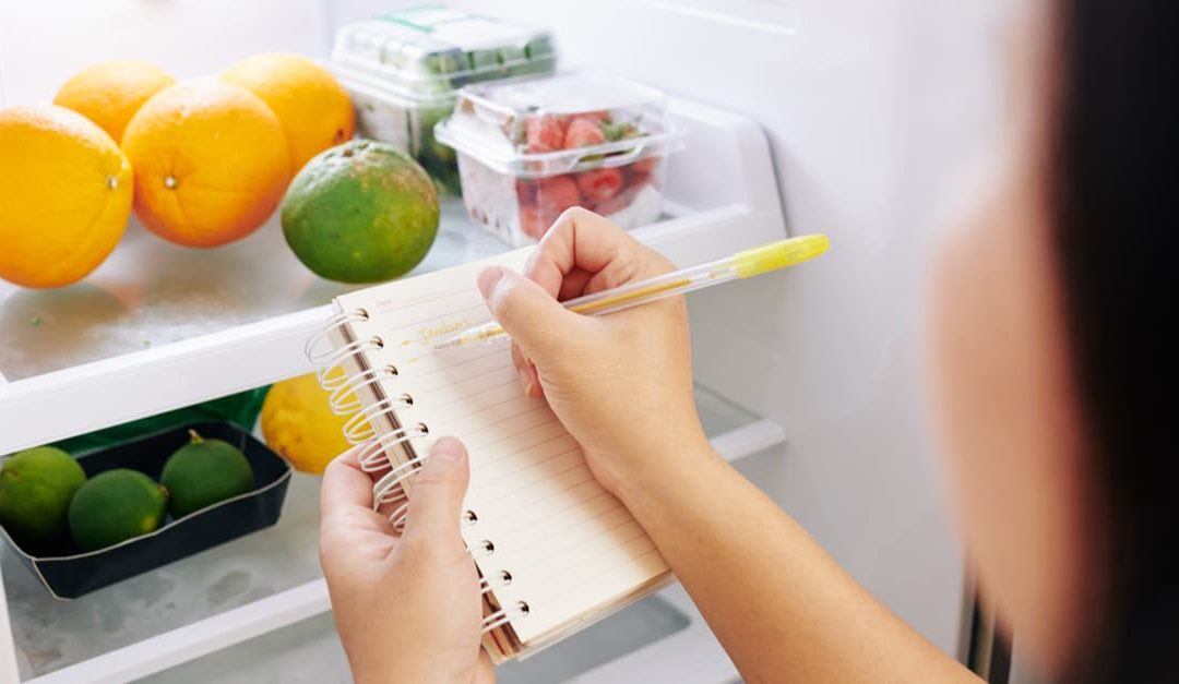 woman writing a vitamin list from the food in her refrigerator