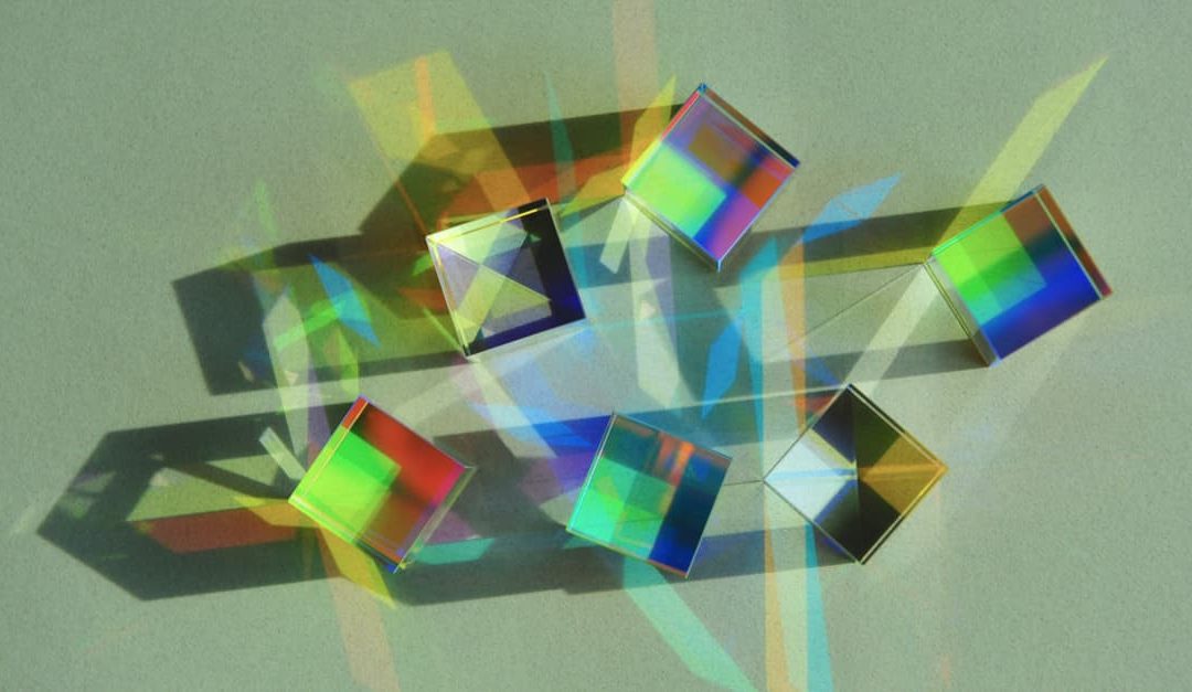 Top view of dichroic glass cube placed in different direction on white paper scattering the strong beam of natural light into colourful spectrums