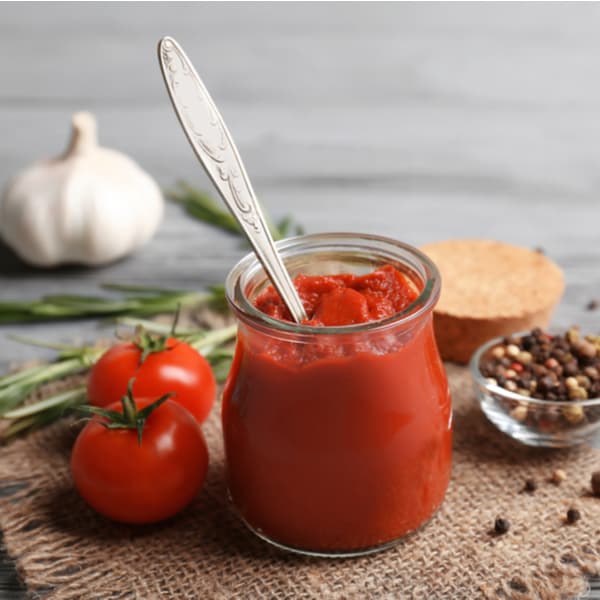 Delicious tomato paste in jar with ingredients on wooden background.